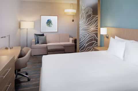 Modern hotel room with queen bed, sofa, and blue accent wall with contemporary artwork