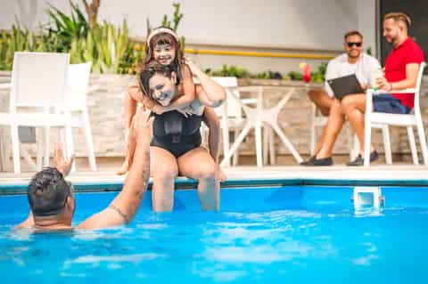 Family enjoying resort pool with children, adults supervising from water and poolside seating