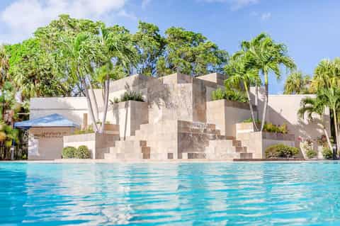 Modern resort pool with geometric concrete wall and palm trees under clear blue sky