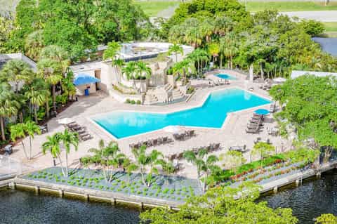 Aerial view of tropical resort with large turquoise pool, palm trees, waterfront gardens, and lounge chairs