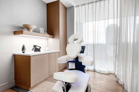 Spa treatment room with white dental chair, wood cabinetry, and sheer curtains overlooking tropical grounds