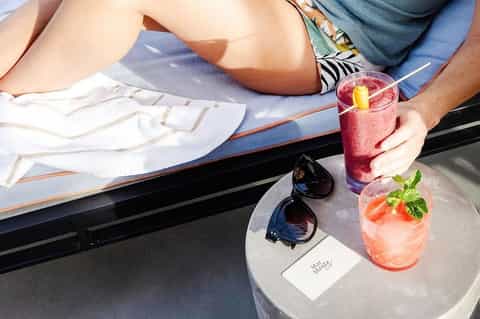Overhead view of two people lounging by pool with colorful cocktails and sunglasses
