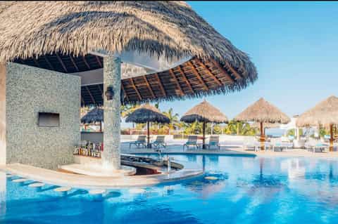 Tropical resort pool bar with thatched roof structures and lounge chairs by crystal blue water