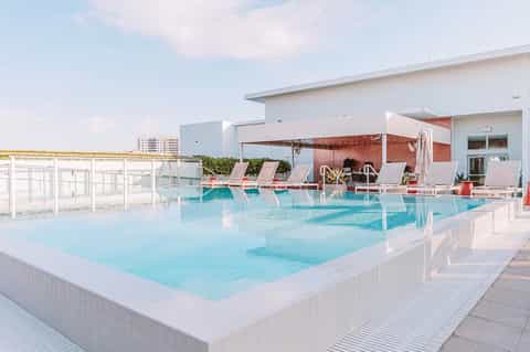 Modern rooftop pool with lounge chairs and red umbrellas, overlooking cityscape on clear day