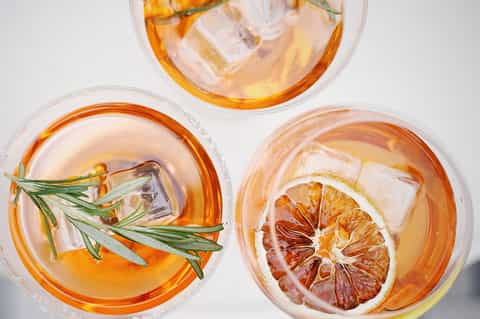 Overhead view of three cocktails with citrus slices, rosemary, and ice in clear glasses