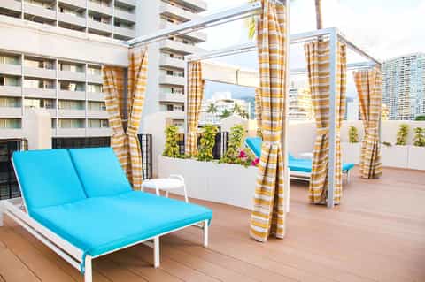 Rooftop deck with bright blue loungers, yellow-striped privacy curtains, and city skyline views