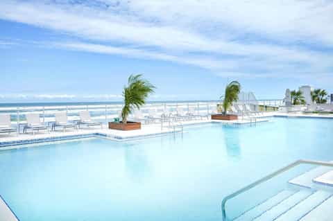 Oceanfront pool deck with lounge chairs, palm trees, and beachside views