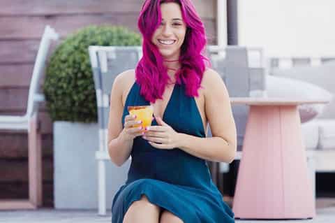 Woman with magenta hair holding a yellow drink on a modern rooftop terrace with lounge areas