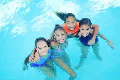 Four smiling children embracing in a bright turquoise swimming pool together