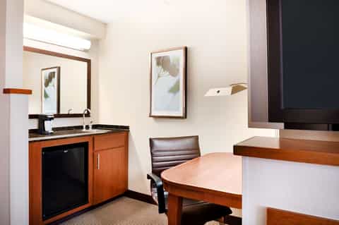 Hotel business center with wooden desk, kitchenette, mirror, and professional workspace