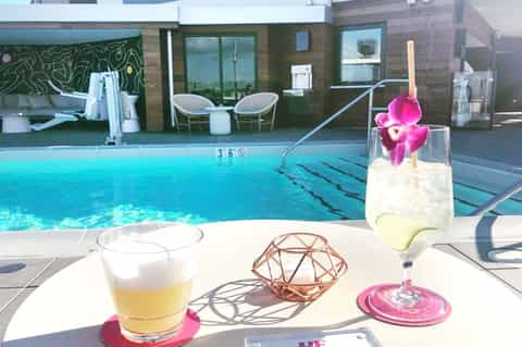 Tropical cocktail with pink flower garnish by resort pool with lounge chairs and building in background