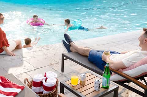 Family enjoying tropical resort beach with turquoise water, lounge chairs, and refreshments on the deck.