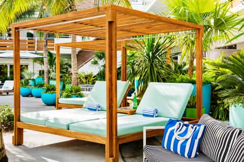 Wooden canopy daybed with white cushions surrounded by tropical plants in resort courtyard