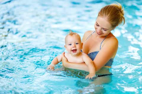 Mother and baby swimming together in bright blue indoor pool