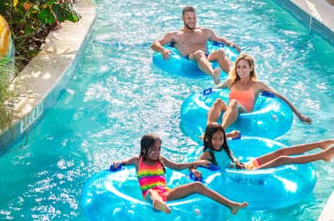 Family enjoying resort pool with blue floats and colorful swimwear on sunny day