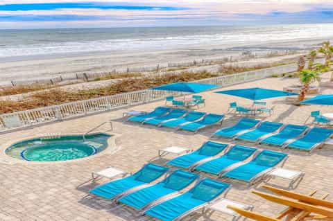 Beachfront resort deck with blue lounge chairs, umbrellas, and ocean view
