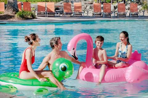 Family enjoying colorful inflatable pool floats in bright turquoise swimming pool