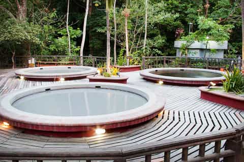 Outdoor spa area with three circular hot tubs on wooden deck surrounded by lush forest landscape