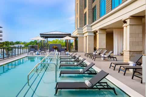 Modern rooftop pool with black loungers, white umbrellas, and city skyline views