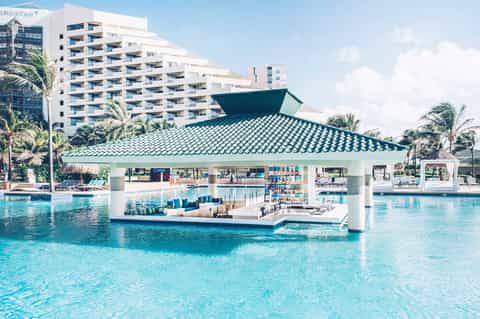Resort pool bar with turquoise water, palm trees, and beachfront hotel