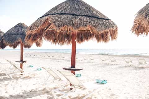 Beach setup with thatched umbrellas, white lounge chairs, and turquoise ocean water