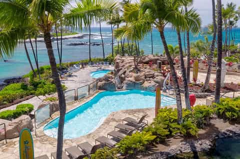 Resort pool surrounded by palm trees with ocean view and lounge chairs