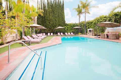 Resort swimming pool with lap lanes, pink and white lounge chairs under umbrellas, tropical landscaping with palm trees