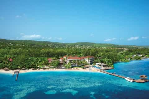 Aerial view of beachfront resort nestled in lush tropical jungle with turquoise waters and white sand beach