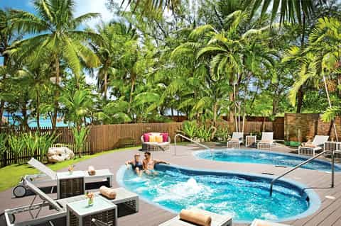 Resort pool area with hot tub, lounge chairs, lush palm trees, and modern outdoor seating