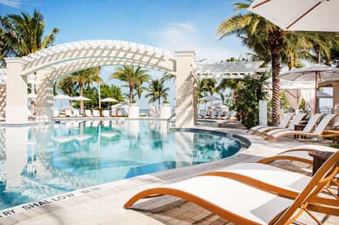 Luxury resort pool with white pergola, palm trees, lounge chairs, and ocean view on sunny day