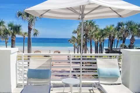Beachfront lounge area with white umbrellas, palm trees, and ocean views under clear blue sky