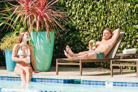 Couple relaxing by resort pool with tropical plants, colorful planters, and lounge chairs in lush garden setting