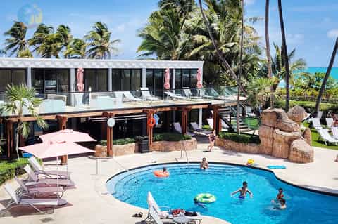 Family-friendly resort pool with water slide, palm trees, lounge chairs, and tropical setting