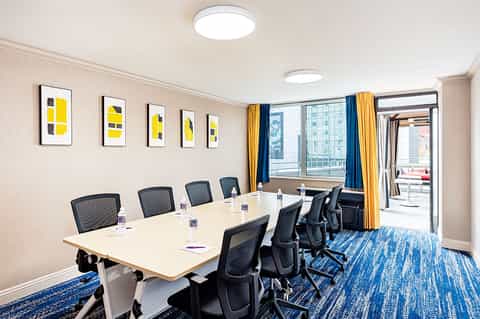 Modern conference room with long white table, black mesh chairs, blue curtains, and city views
