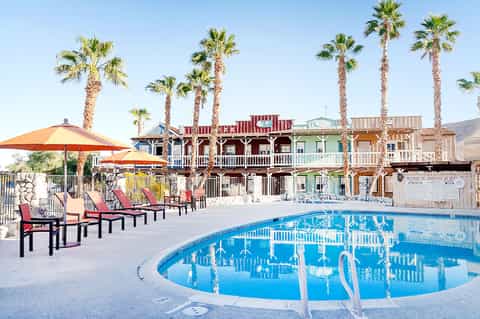 Resort pool area with colorful Western-style building, palm trees, lounge chairs, and bright blue pool