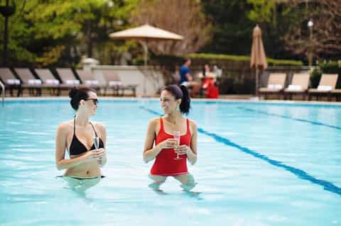 Two women enjoying drinks in a resort swimming pool surrounded by lounge chairs
