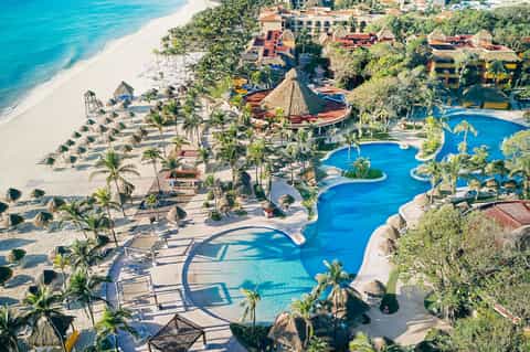 Aerial view of beachfront resort with curved pools, palm trees, and sandy beach