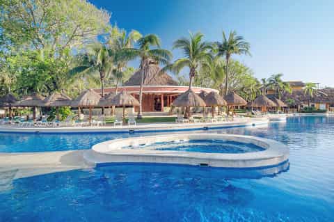 Beachfront resort with tiki umbrellas, pool, and tropical palm trees under clear sky