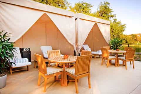 Outdoor glamping setup with peaked canvas tents, wooden furniture, and lounge chairs on patio