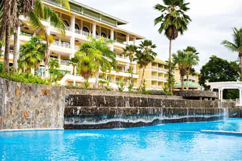 Tropical resort building with yellow exterior, palm trees, and blue swimming pool