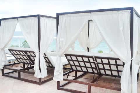 Beachfront cabana beds with white curtains and ocean view on a sandy patio