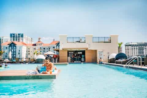 Man relaxing on floating platform in resort pool with waterfront buildings