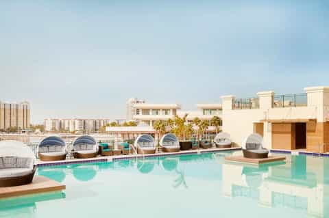 Luxury resort rooftop pool with white cabanas, palm trees, and high-rise building backdrop during daytime