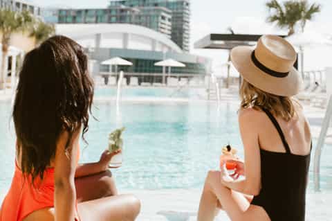 Two women relaxing poolside with cocktails at modern resort