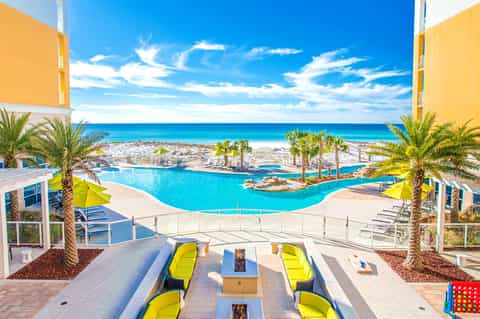 Resort pool overlooking turquoise ocean with palm trees and yellow umbrellas