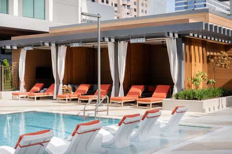 Resort pool deck with orange lounge chairs, cabanas, and modern building architecture