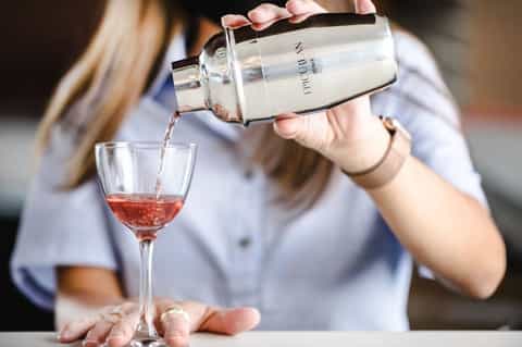 Bartender pouring red cocktail from shaker into glass