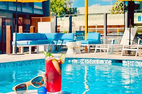 Colorful cocktail by resort pool with blue lounge seating and yellow umbrellas in background