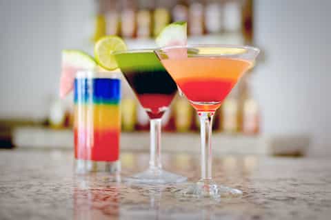Three colorful layered cocktails with lime slice and garnish on counter