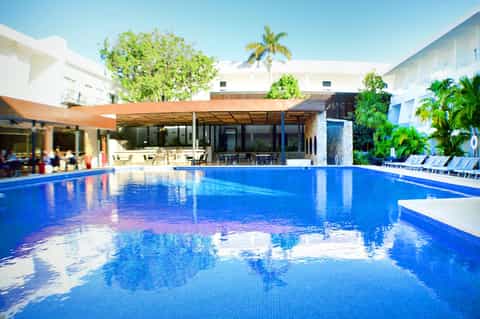 Resort swimming pool with bright blue water, white umbrellas, and modern white building with palm trees